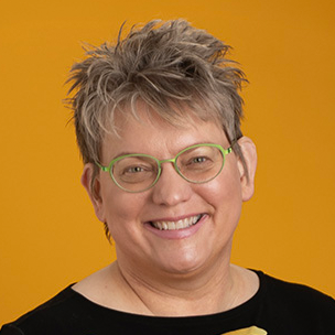Kerri Husman is a Caucasian woman with short hair and blue eyes. She is wearing green rimmed glasses and smiling at the camera.