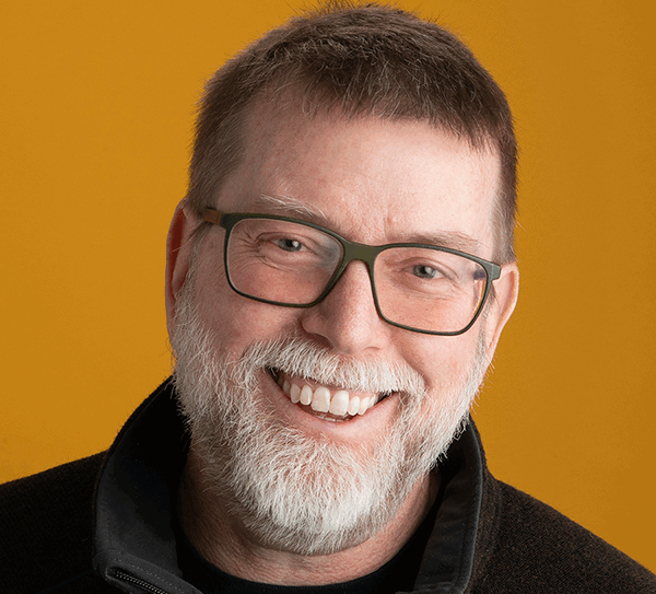 Todd Leach is a Caucasian man with gray hair and a silver gray beard. He is wearing dark rimmed glasses and smiling at the camera.