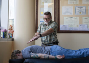 Todd providing field repatterning - Mammoth Hills Coaching and Wellness, LLC A middle aged man providing healing touch field repatterning over the back of a woman lying down face down on a massage table