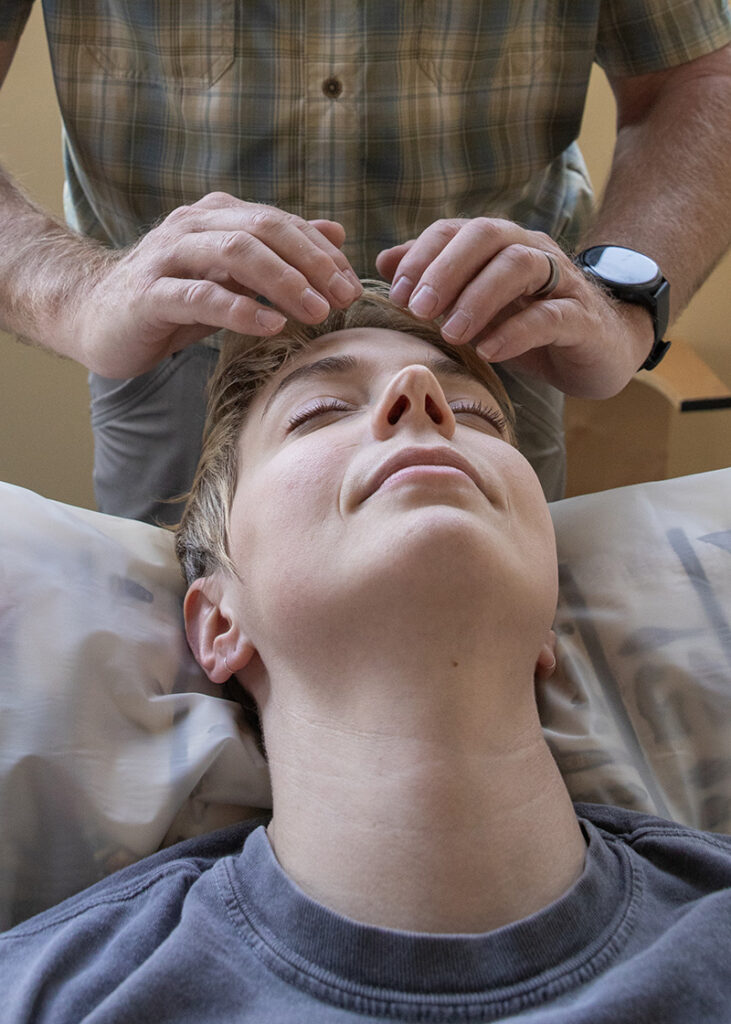 Todd providing Healing Touch - Mammoth Hills Coaching and Wellness, LLC A man is offering Noel's Mind clearing over the brow chakra of a female client resting comfortably. His hands are in a "v" pattern over her forehead