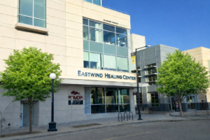 Eastwind outside with AI tree_sign edit - Mammoth Hills Coaching and Wellness, LLC Exterior of Eastwind Healing Center from Linn Street. There is a side entrance on Linn Street and on College Street around the cornder. The Eastwind name is on the 2nd floor above Formosa restaurant, and there are green trees on either side.