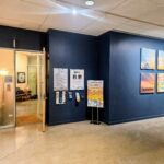 Interior hallway of a healing center with dark blue walls, framed posters on the right, and an open doorway to a warmly lit waiting area on the left.