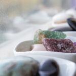 Colorful crystals or minerals arranged in white bowls on a bright windowsill.