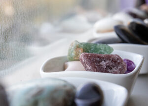 stones - Mammoth Hills Coaching and Wellness, LLC Colorful crystals or minerals arranged in white bowls on a bright windowsill.